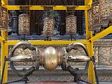 Kathmandu Patan Golden Temple 08 Vajra And Prayer Wheels An enormous vajra is flanked by prayer wheels just inside the entrance to Golden Temple in Patan. The Swaymbhu Chaitya is behind.